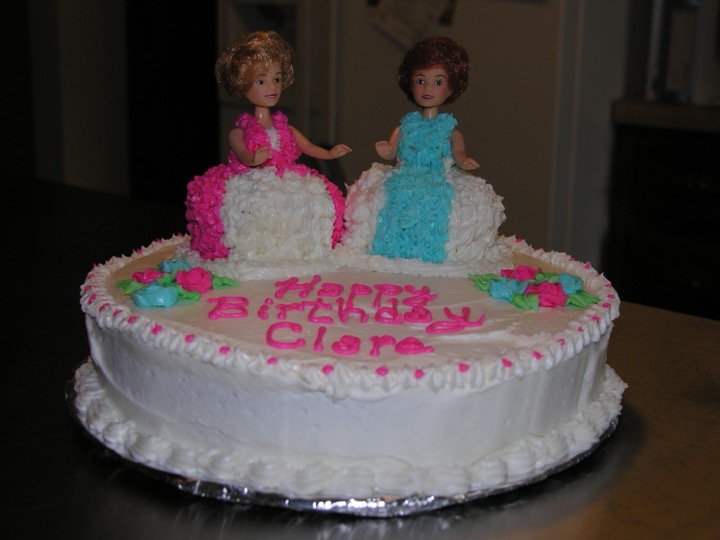 White birthday cake with two doll toppers and icing dresses