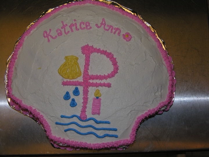 Shell-shaped baptism cake with cross, seashell, and water droplet piping