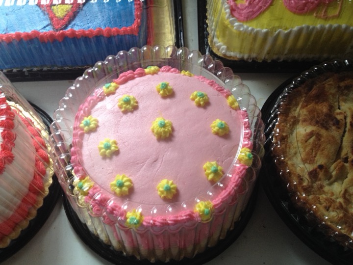 Pink round cake with yellow buttercream flowers beside other packaged cakes
