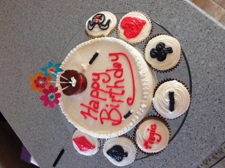 White birthday cake with magic-themed cupcakes featuring card suits and a rabbit