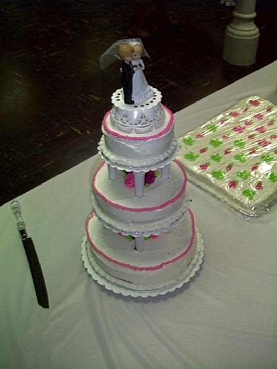 Three-tier white wedding cake with pink accents and bride-and-groom topper